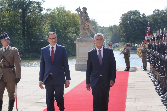 Premier Morawiecki i premier Babisz idą po czerwonym dywanie, po lewej i prawej stronie stoją żołnierze pełniący wartę honorową.
