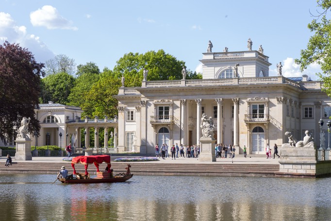 Widok na Pałac na Wyspie, przed Pałacem stoją ludzie, po wodzie pływa gondola.