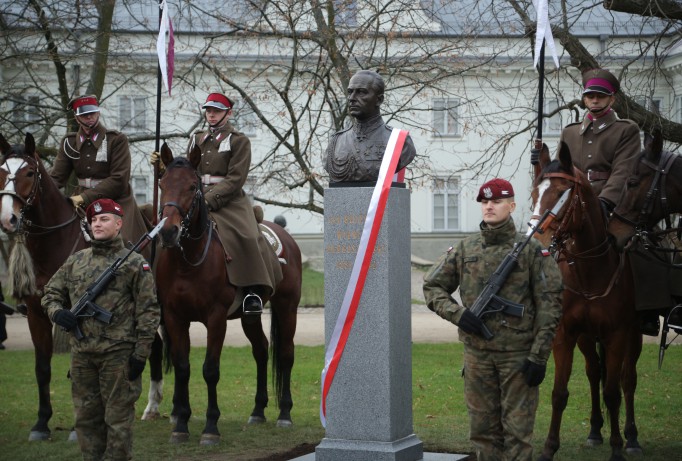 Pomnik Bolesława Wieniawy-Długoszowskiego ozdobiony biało-czerwoną wstęgą, przy pomniku stoją żołnierze, trzech z nich siedzi na koniach.