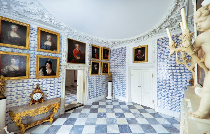 Jedna z sal Pałacu na Wyspie, na ścianach której wiszą portrety, po lewej stronie po ścianą stoi stolik, na którym znajduje się ozdobny zegar.