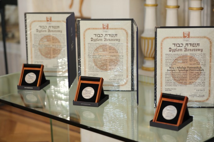 Trzy medale "Sprawiedliwy wśród Narodów Świata" stojące na szklanej półce na tle trzech dyplomów. 