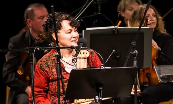 Muzycy na scenie podczas koncertu, trzymają instrumenty smyczkowe. 