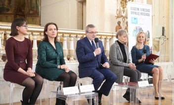 Kobieta, mężczyzna i dwie kobiety siedzą obok siebie na krzesłach. 
