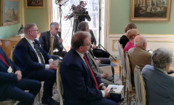 Ludzie siedzą na krzesłach w sali Pałacu Myślewickiego. 