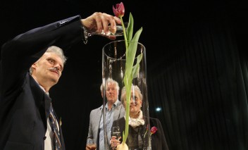 Chrzest tulipana. Do wazonu, w którym stoi kwiat mężczyzna wlewa szampana z kieliszka.