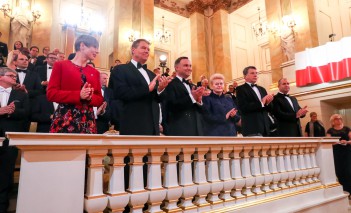 Ludzie stoją w loży teatralnej i klaszczą w dłonie.