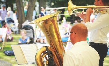 Dwaj mężczyźni grają na instrumentach w łazienkowskich ogrodach, w tle widać słuchaczy. 