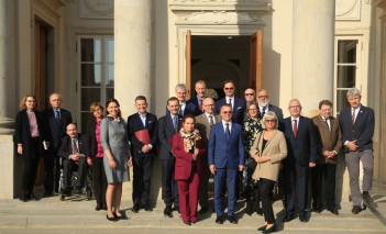 Grupa osób stoi na schodach przed Pałacem na Wyspie i pozuje do zdjęcia.