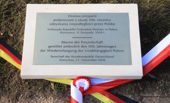Tablica pamiątkowa z napisem i widocznymi u dołu szarfami.