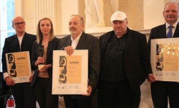 Trzech mężczyzn pozuje do zdjęcia, mężczyźni z lewej i prawej strony trzymają w rękach dyplomy.