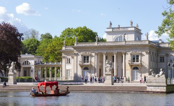 Widok na Pałac na Wyspie, przed Pałacem stoją ludzie, po wodzie pływa gondola.