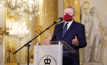 Minister kultury na konferencji prasowej, przemawiający przed mikrofonem. 