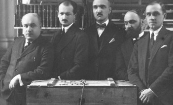 Pięciu mężczyzn w garniturach na archiwalnej fotografii, stojących przy skrzyni,