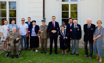 Grupa powstańców pozuje do zdjęcia na tle fasady Pałacu Myślewickiego.
