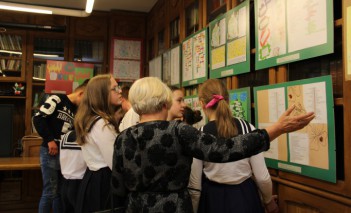 Uczniowe i nauczycielka przed tablicą z planszami edukacyjnymi.