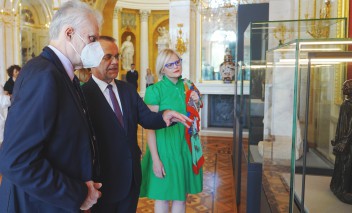 Dwóch mężczyzn w garniturach i kobieta w zielonej sukience stoją w Sali Salomona w Pałacu na Wyspie przed szklaną gablotą.