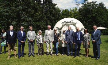 Grupa osób stojąca w rzędzie w łazienkowskich ogrodach przed rzeźbą w kształcie kuli. 