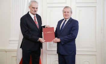 Dwaj mężczyźni w garniturach stoją obok siebie, trzymając przed sobą czerwoną kartę. 