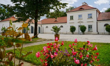 Budynek Stajni Kubickiego. Przed budynkiem na trawniku rosną czerwone kwiaty. 