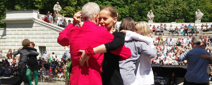 Kobiety i mężczyźni w parach tańczą na plenerowej scenie. 