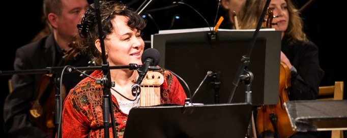 Muzycy na scenie podczas koncertu, trzymają instrumenty smyczkowe. 
