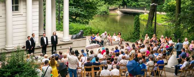 Grupa osób siedzi przed Świątynią Sybilli i słucha koncertu.