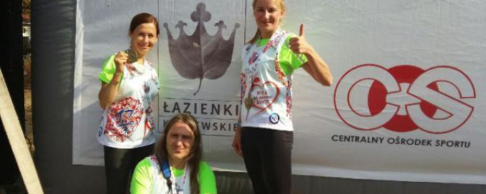 Dwie kobiety stoją i unoszą kciuki, trzecia kuca.
