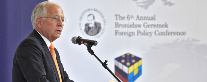 Mężczyzna stoi przed mikrofonem, opiera dłonie o pulpit i przemawia.