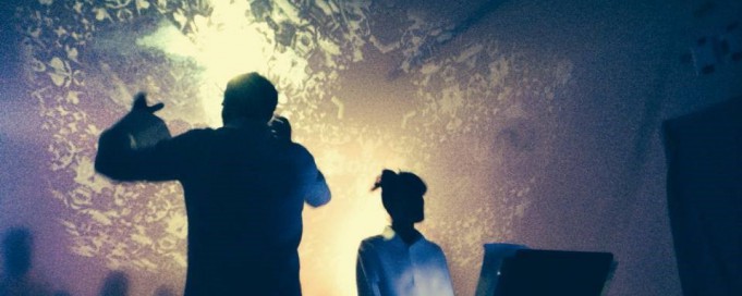 Przedstawienie teatralne, mężczyzna stoi tyłem, unosząc ręce, kobieta przodem śpiewa.