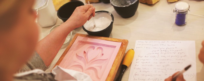 Kobieta przygotowuje gipsowy odlew, mieszając gips w misce, przed nią leży forma do wylewu masy gipsowej.