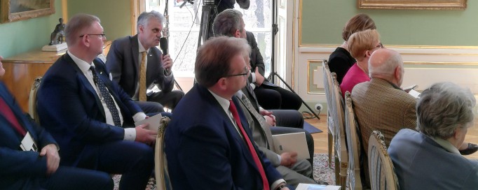 Ludzie siedzą na krzesłach w sali Pałacu Myślewickiego. 
