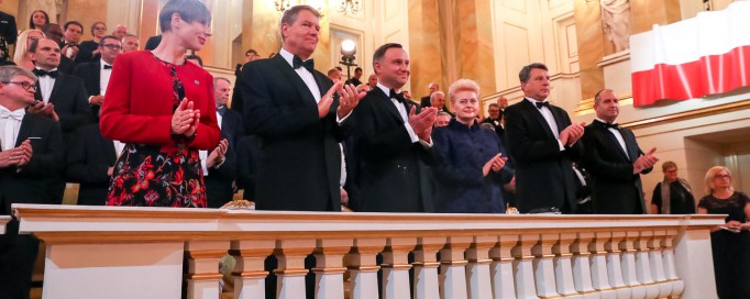 Ludzie stoją w loży teatralnej i klaszczą w dłonie.