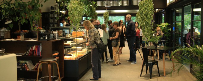 Wnętrze kawiarni, grupa osób stoi przed ladą.