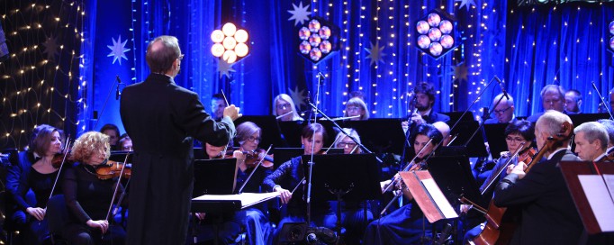 Mężczyzna dyryguje orkiestrą grającą na scenie.