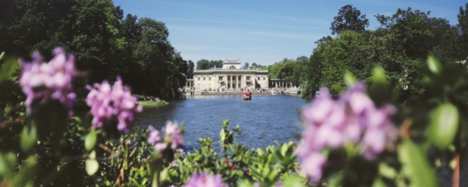 Widok na Pałac na Wyspie w otoczeniu wody, drzew i kwiatów. 