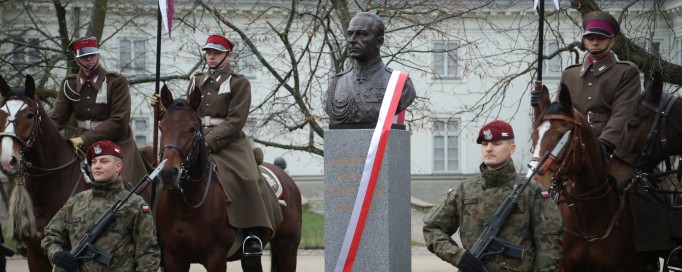 Pomnik Bolesława Wieniawy-Długoszowskiego ozdobiony biało-czerwoną wstęgą, przy pomniku stoją żołnierze, trzech z nich siedzi na koniach.
