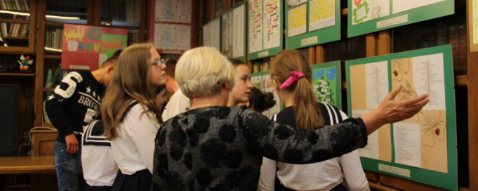 Uczniowe i nauczycielka przed tablicą z planszami edukacyjnymi.