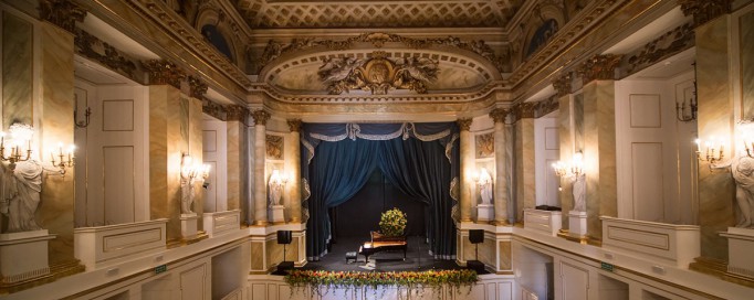 Wnętrze Teatru Królewskiego w Starej Oranżerii, widoczna jest scena, na której stoi fortepian.