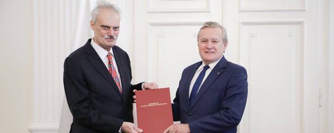Dwaj mężczyźni w garniturach stoją obok siebie, trzymając przed sobą czerwoną kartę. 