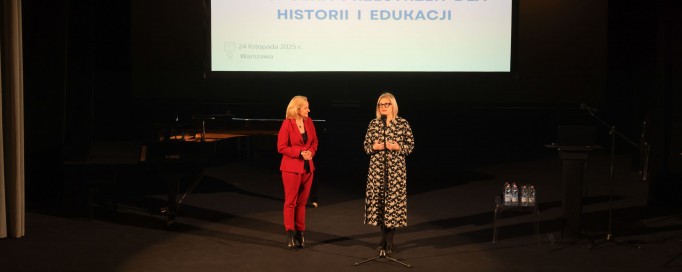 Dwie kobiety stoją na scenie. Kobieta po lewej jest ubrana w czerwone spodnie i marynarkę, a kobieta po prawej w czarną sukienkę w białe wzory. Powyżej, nad ich głowami, wisi plansza z napisem "Muzealnictwo i izby pamięci - wspólna przestrzeń dla historii"