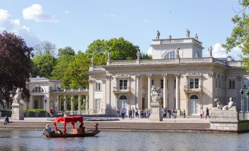 Widok na Pałac na Wyspie w otoczeniu drzew i wody.