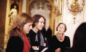 Trzy kobiety stoją w pałacowej sali.