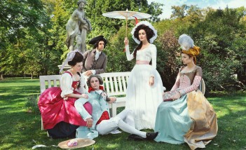 Kobiety i mężczyźni w strojach z epoki pozują do zdjęcia w ogrodach Łazienek Królewskich.