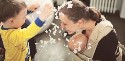 Dziecko obsypuje kobietę, która kuca, trzymając niemowlę, białymi kawałkami papieru.