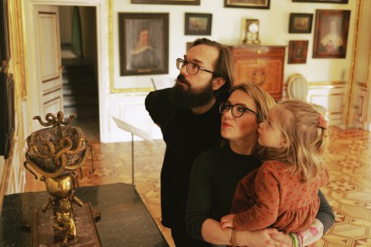 Mężczyzna oraz kobieta z dzieckiem na ręku zwiedzają pomieszczenie Pałacu Myślewickiego.