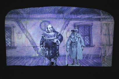 Kadr z spektaklu "Barani Kożuszek". Widać lalki z papieru, przedstawiające dwóch mężczyzn na tle ściny domu. 