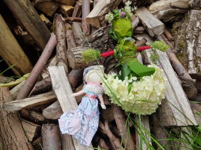 Dwie ręcznie wykonane lalki, jedna zielona, druga biała, leżą na stosie patyków. 