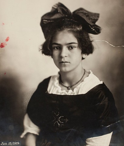 Portret młodej dziewczyny z dużą kokardą na głowie, ubranej w białą i czarną bluzkę, z naszyjnikiem na szyi. 