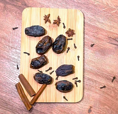Daktyle, pałeczki cynamonu i gwizdki anyżu leżące na drewnianej desce do krojenia. 