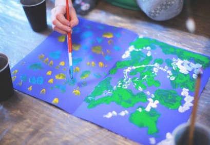 Dłoń dziecka malująca na ciemnym papierze kolorowe plamki. 